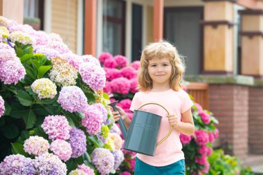 Çocuk yazın güneşli bir günde bahçede çiçek suluyor. Bahçede çiçekleri sulamak. Kırsal kesimde yaşayan çiftçi çocuklar. Bahçede çiçekleri sulayan sevimli küçük çocuk..