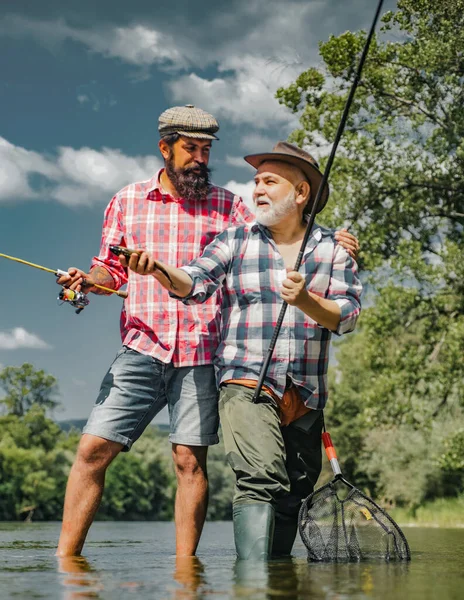 Nonno e ragazzo pescano insieme. Buon padre e figlio pesca in fiume tenendo canne da pesca. Pesce trota fario. Padre e figlio pesca. — Foto Stock