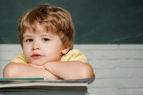 Okul malzemeleriyle masasının yanında duran mutlu yüzlü bir öğrenci. Çocuk arkaplanda bir tahtayla cevap vermeye hazır. Öğretmenler Günü. — Stok fotoğraf
