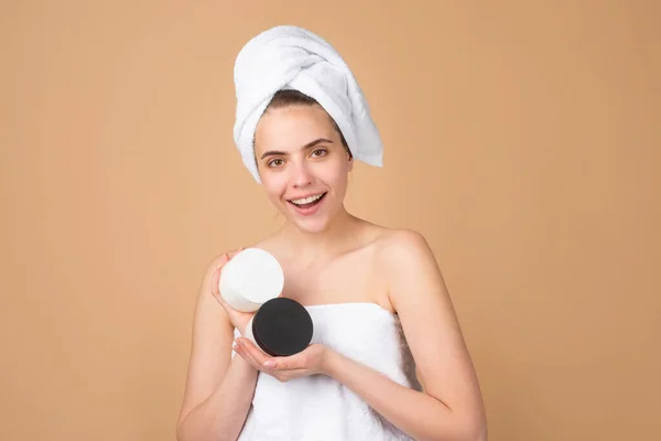 Hermosa chica feliz con botella de crema, limpia la piel fresca. Tratamiento facial. Cosmetología belleza y spa. Chica aplicar crema para el cuidado de la piel en la cara. Gestos para publicidad. Fondo beige —  Fotos de Stock