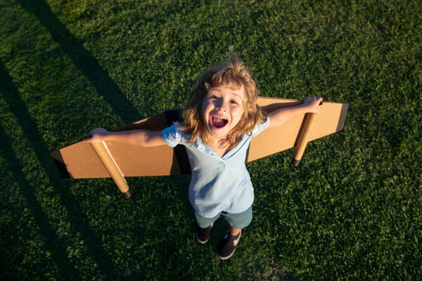 Opgewonden kind met rugzakvleugels. Een kind dat piloot speelt en buiten droomt in het park. Glimlachend kind droomt over zomervakantie en reizen. Jongen droomt van vliegen. Zorgeloos buiten spelend kind. — Stockfoto