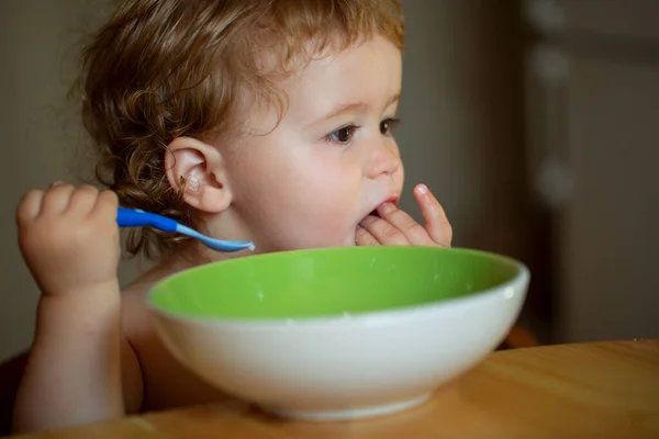 Vtipné dítě jíst jídlo sám s lžící na kuchyni. — Stock fotografie