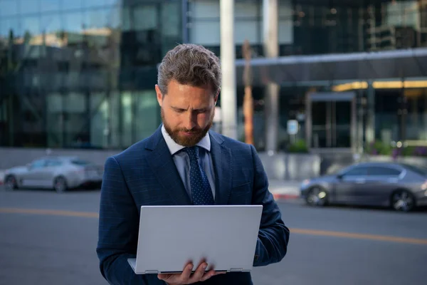 Geschäftsmann mit Laptop steht auf der Straße in der Nähe eines Bürogebäudes. — Stockfoto