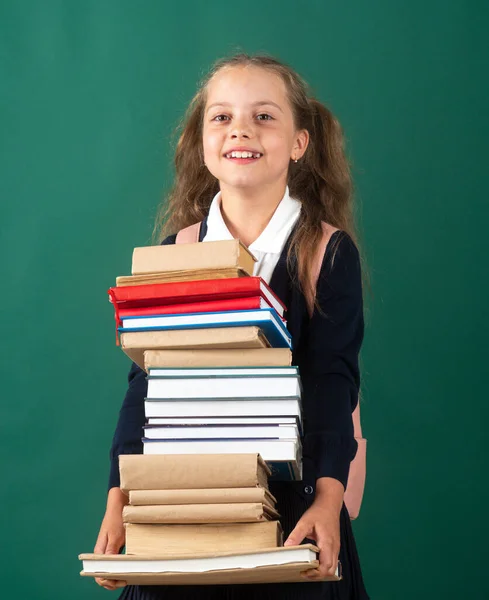 Sonriente niña escolar divertida con mochila sostiene libros en pizarra verde. Concepto de estilo de vida infantil. Educación en la escuela. Día del conocimiento. —  Fotos de Stock