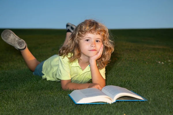 Школьник с книгой отдыхает на свежем воздухе. Умный мальчик читает книгу, лежа на траве и фоне неба с копировальным пространством. — стоковое фото