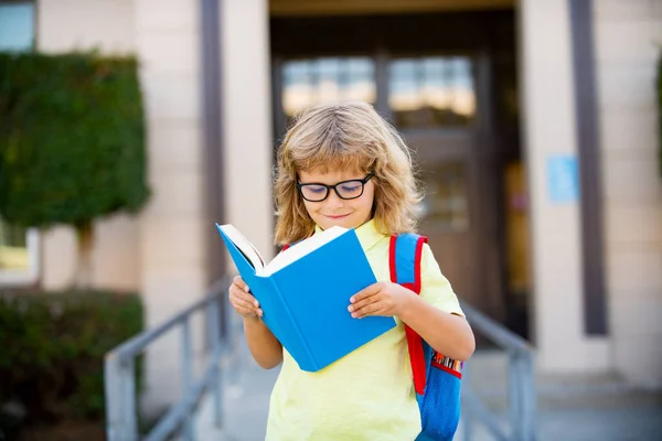 Petit garçon joyeux avec grand sac à dos et livre s'amuser contre l'école. Je retourne à l'école. Concept d'éducation et de lecture. — Photo