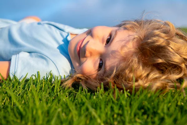 Porträtt av en leende liten pojke som ligger på grönt gräs och drömmer. Söta barn njuter av naturen utomhus. Friska bekymmerslös unge leker ute i sommarparken på en gräsmatta. — Stockfoto