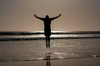 Sahilde zıplayan bir adamın silueti. Gün batımı kumsalında inanılmaz manzara.
