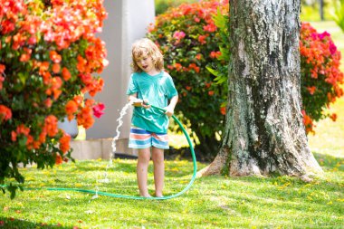 Bir yaz akşamı evin arka bahçesindeki su hortumuyla çiçekleri sulayan sevimli bir çocuk..
