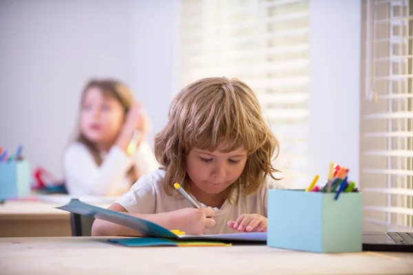 Porträtt av pojken som tecknar i copybook. Skolungen skriver något i copybook och sitter vid bordet i klassrummet. Koncentrerade skolbarn ockuperade. — Stockfoto