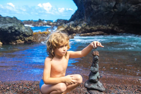 かわいい少年は、自然の中で海の海岸に積層石を作る。海のビーチで、 5つの小石の塔ケルン。バランスと調和の概念。落ち着きと精神. — ストック写真