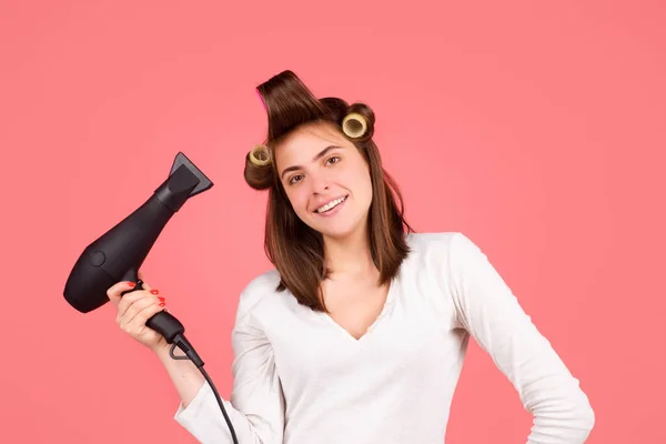 Mujer sonriente con secador de pelo. Hermosa chica feliz con el pelo liso y rodillos secar el cabello con secador de pelo profesional. — Foto de Stock