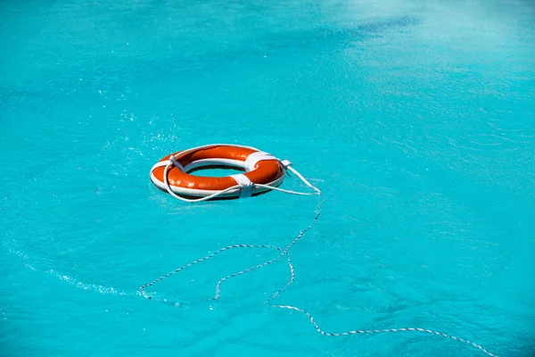 海やプールのライフベルト。青い水に浮かぶオレンジ色のインフレータブルリング。保護と安全溺死のための生活ブイ. — ストック写真