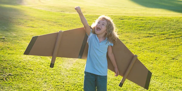 Barn leker med leksaksvingar i sommarparken. Innovation och framgångskoncept. Kid pilot har kul på gräs i parken. Glada barn leker utomhus. — Stockfoto