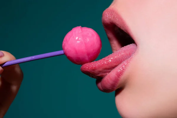 Dilini yalıyor. Ağzında kırmızı lolipop şekeri tutan pembe rujlu yakın plan kadın dudakları. Lolipop dudaklı kadın yüzü. — Stok fotoğraf