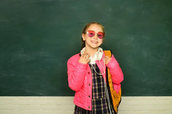 Sırt çantalı genç liseli kız. Genç bir kız öğrencinin portresi. Gözlüklü komik liseli kız. Eğitim konsepti. Okul çantası ve kulaklığı olan genç bir kız öğrenci.. — Stok fotoğraf
