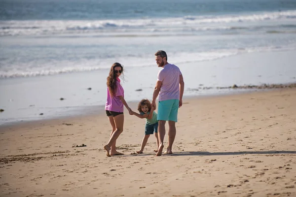 幸せな若い家族が走り、夏のビーチでジャンプします。自然の海に親を持つ子供。幼少期と育児の概念. — ストック写真