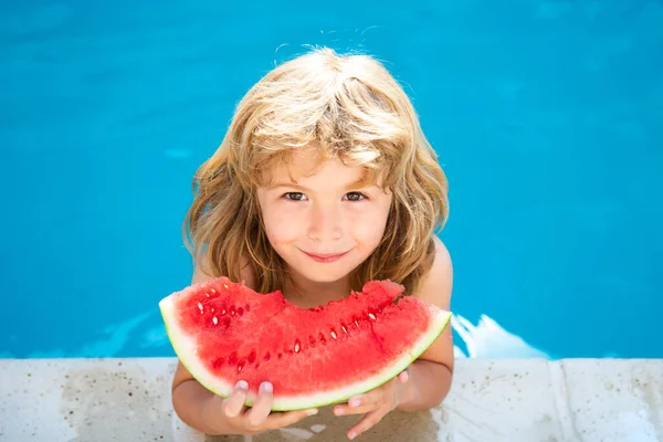 Barn äter vattenmelon nära poolen under sommarlovet. Barn äter frukt utomhus. Hälsosam mat för barn. Liten pojke leker i poolen med en skiva vattenmelon. — Stockfoto