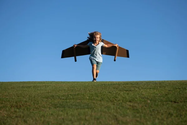 Niño jugando con alas de avión de juguete en el parque de verano. Innovación tecnológica y concepto de éxito. Aviador piloto infantil con sueños de avión de viajar en verano en la naturaleza. — Foto de Stock