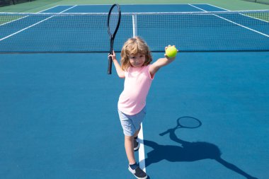 Sahada tenis oynayan çocuk. Spor kulübünde tenis raketi ve topu olan küçük bir kız. Çocuklar için aktif egzersiz. Çocuklar için yaz etkinlikleri. Küçük çocuk için antrenman..