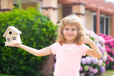 Mutlu çocuk yeni evine karşı oyuncak evi elinde tutuyor. Çocuklar için konut kavramı.