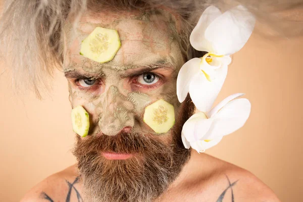 Funny man with clay mask and cucumber slices on face. Male spa, dermatology, wellness and facial treatment concept. Man having cosmetic moisturizing mask, isolated studio background. Male face care. — Stock Photo, Image