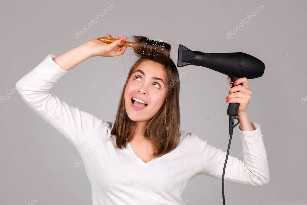 Funny woman with hair dryer. Beautiful girl with straight hair drying hair with professional hairdryer.