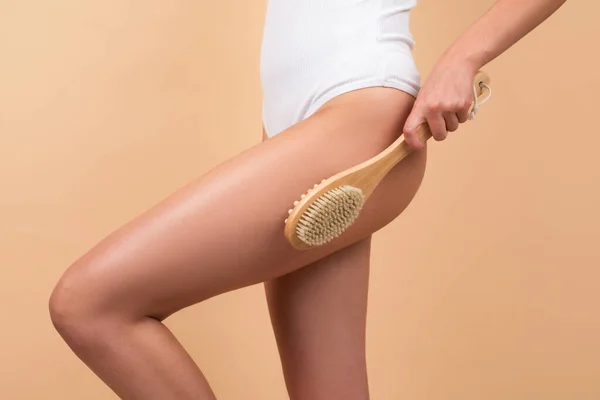 Woman legs with clean skin. Female buttocks ass without cellulite. Skin treatment. Cosmetology, spa cosmetic products, beauty close-up. Woman makes massage with a wooden soft massage brush for body. — Stockfoto