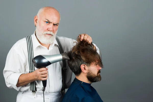Uomo barbuto che viene curato dal parrucchiere con asciugacapelli presso il barbiere. Serios parrucchiere in possesso di un asciugacapelli. — Foto Stock