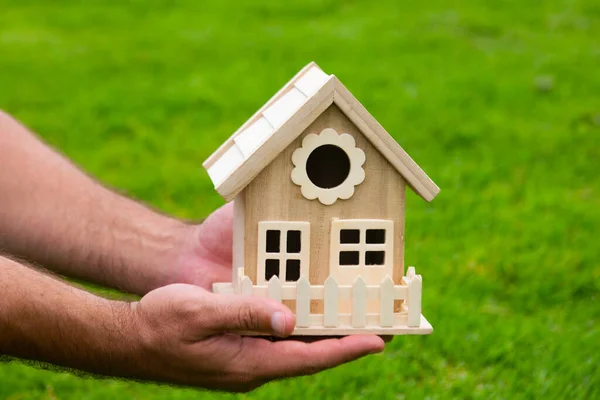 Mano masculina sosteniendo el modelo de casa de cerca. Pequeña casa de juguete en miniatura. Hipoteca propiedad sueño mudanza casa y concepto de bienes raíces. — Foto de Stock
