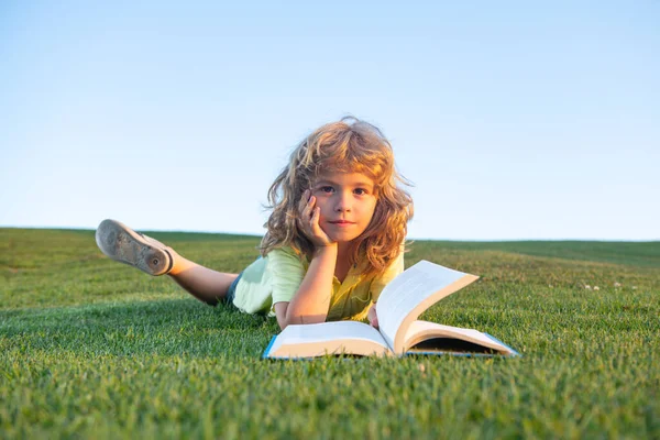 Забавный парень, читающий книгу в весеннем парке. Ребенок читает книгу о весеннем парке. Отдых на траве в саду. Образование на природе. — стоковое фото