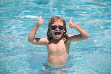 Yaz yüzme havuzunda bir çocuk. Başparmakları havada, yüzme havuzunda yüzen tatlı çocuk, fotokopi alanı olan yaz suyu arka planı. Komik çocuk suratı. Başparmaklar yukarı..