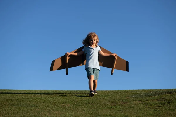 Criança voando em avião feito artesanato de asas de papelão. Sonho, imaginação, infância. Conceito de viagem e férias de verão. Jovem piloto contra um céu azul com cópia cpase. — Fotografia de Stock