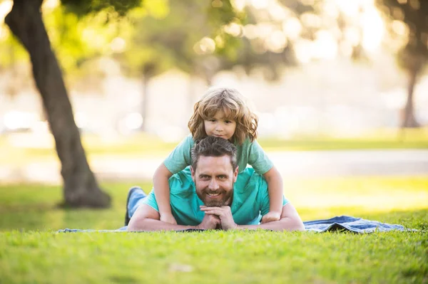 Papá con niño lindo acostado en la hierba en el parque de verano al aire libre. Padre e hijo relajándose en la naturaleza. — Foto de Stock