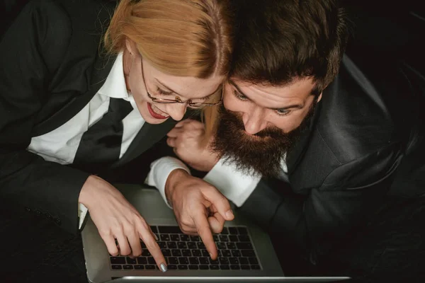 Mulher de negócios jovem e empresário bonito em ternos estão usando um laptop no quarto escuro. Retrato de um casal de negócios espantado olhando para computador portátil isolado em preto. — Fotografia de Stock