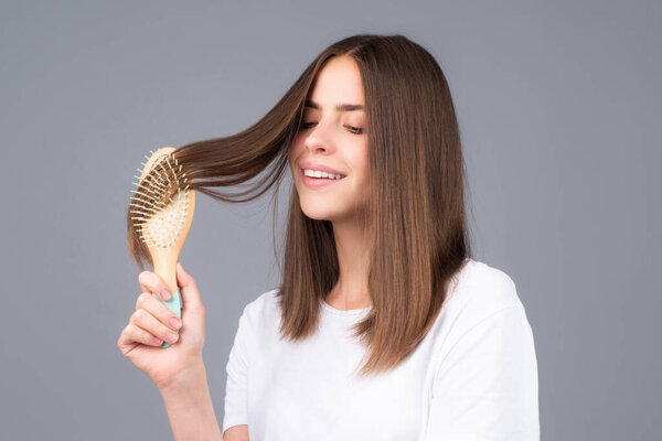 Brushing Hair. Portrait young smiling woman brushing straight natural hair with comb. Girl combing hair with hairbrush. Hair care beauty concept.