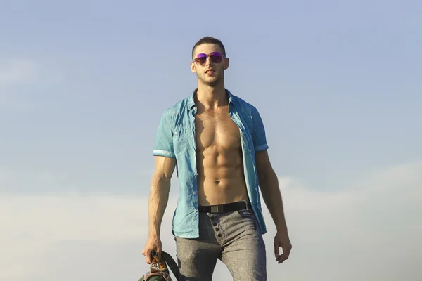 Trendy guy in sunglasses and a blue shirt against the sky — Stock Photo, Image