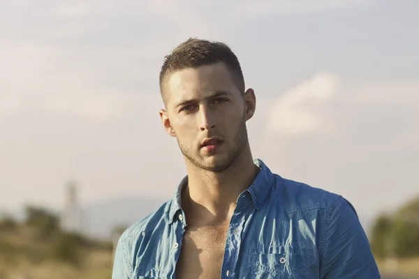 Primer plano del joven guapo mirando a la cámara contra el cielo — Foto de Stock