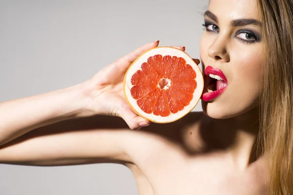 Гламурная девушка держит грейпфрут и подтягивает его губами. — стоковое фото