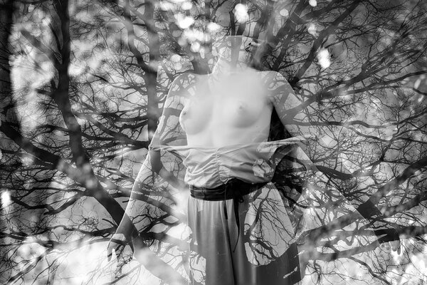 Sensual pretty young naked girl with beautiful bosom standing thowing head back with bare tree branches texture on natural background black and white, horizontal picture