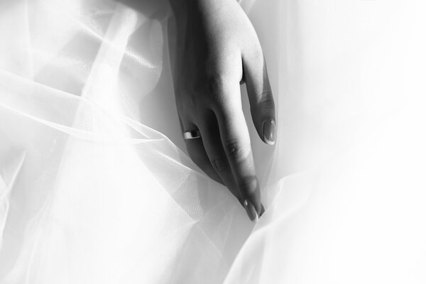 Closeup of female hand with beautiful wedding ring from precious metal on haze fabric of bridal dress black and white, horizontal picture