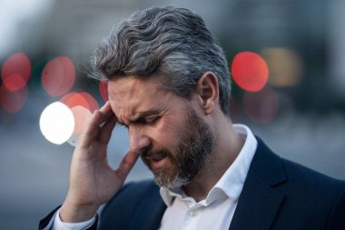 Dışarıda baş ağrısı çeken yorgun bir iş adamı. Takım elbiseli bir adam ağrıyı dindiriyor, migren. İş sorunları. İflas, mali sorun ve kriz konsepti. Milenyum adamı baş ağrısı çekiyor. Migren..