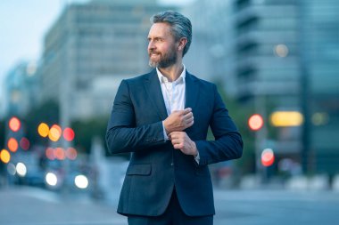 Şehir caddesinde başarılı bir orta yaşlı işadamı duruyor. Takım elbiseli bir adam açık şehir gece portresi. Olgun bir iş adamı şehirde yürüyor. Şehir caddesinde poz veren bir ofis çalışanı