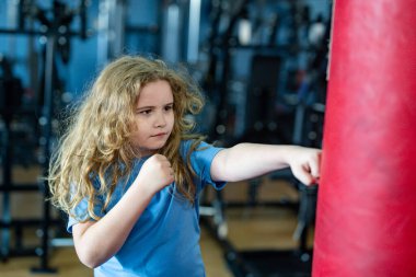 Eğitimdeki boksör çocuk. Eldivenle çocuk yumruklamak. Genç boksör antrenmanı. Sportif çocuk torbaya vurdu. Güçlü gençlik iş başında. Çocuk kickboks antrenmanı yapıyor. Aktif çocuk dövüşçüsü portresi