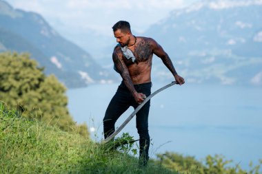 Çiftlikte çalışan kırsal kesimden güçlü bir adam. Güneşin altındaki bir tarlada çalışan çiftçi. Çimenli bir tarlada tırmık ve yaba ile çiftçi. Yeşil bir alanda kırsal bir işçi. Kırsal kesimdeki çalışkan adam.