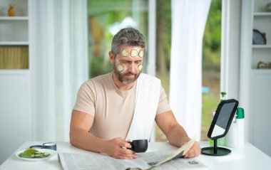 Orta yaşlı bir adam evde sabah cilt kremi sürerken yüz kremi sürüyor. Olgun bir adam yaşlanmayı ve gençleşmeyi önlemek için nemlendirici bir maske kullanıyor. Erkek kozmetik yüz tedavisi