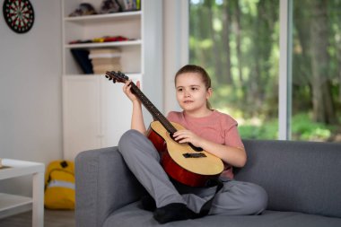 Gitar çalan çocuk. Çocuk oturma odasında gitar çalma alıştırması yapıyor. Çocuk içeride gitar öğreniyor. Müzik dersi sırasında gitarlı bir çocuk. Akustik gitar çalan bir çocuk. Çocuk şarkıları çalışıyor
