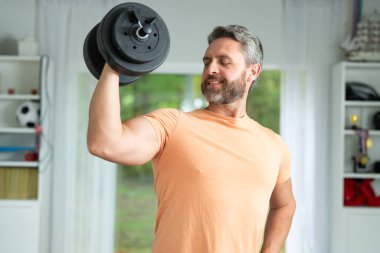 Latin adam evde egzersiz yapmak için ağırlık kaldırıyor. Sporcu oturma odasında güçlü pazılar için egzersiz yapıyor. Biceps kıvırcık. Olgun erkek pazıları. Sağlıklı bir adam ağırlık kaldırıyor.