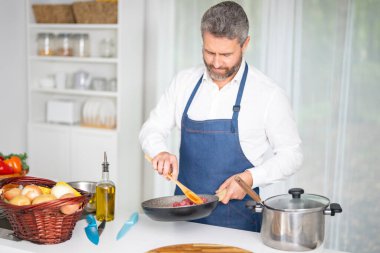 Taze sebze pişiren bir şef. Ev yapımı yemek pişiren bir adam. Mutfakta sağlıklı bir kahvaltı için sebze pişiren bir aşçı. Modern bir mutfakta sebze pişiren üniformalı bir adam.