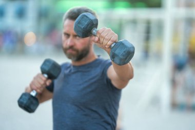 Olgun bir adamın dambılları dışarı kaldırırken yakın çekimi. Olgun adamların kol kasları halter egzersizi yapıyor. Kol halterine yakın çekim. Dambılı formda bir erkek kolunun yakın çekimi.